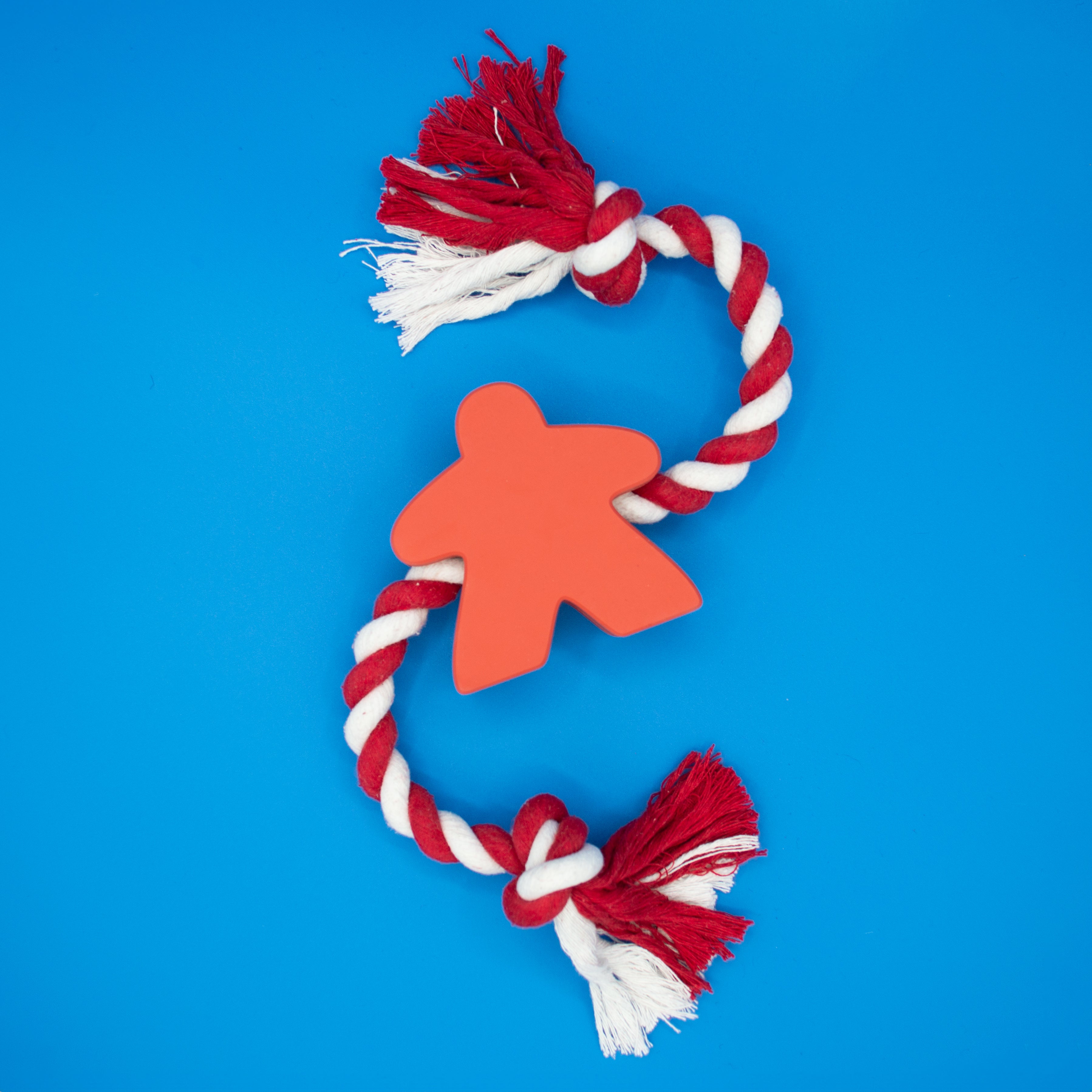 Red rubber meeple dog toy with red and white rope on blue background